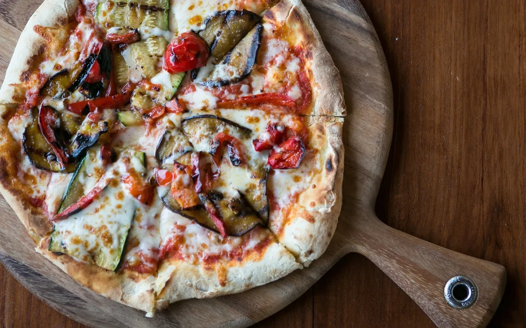 Freshly baked pizza with roasted vegetables on a wooden peel.