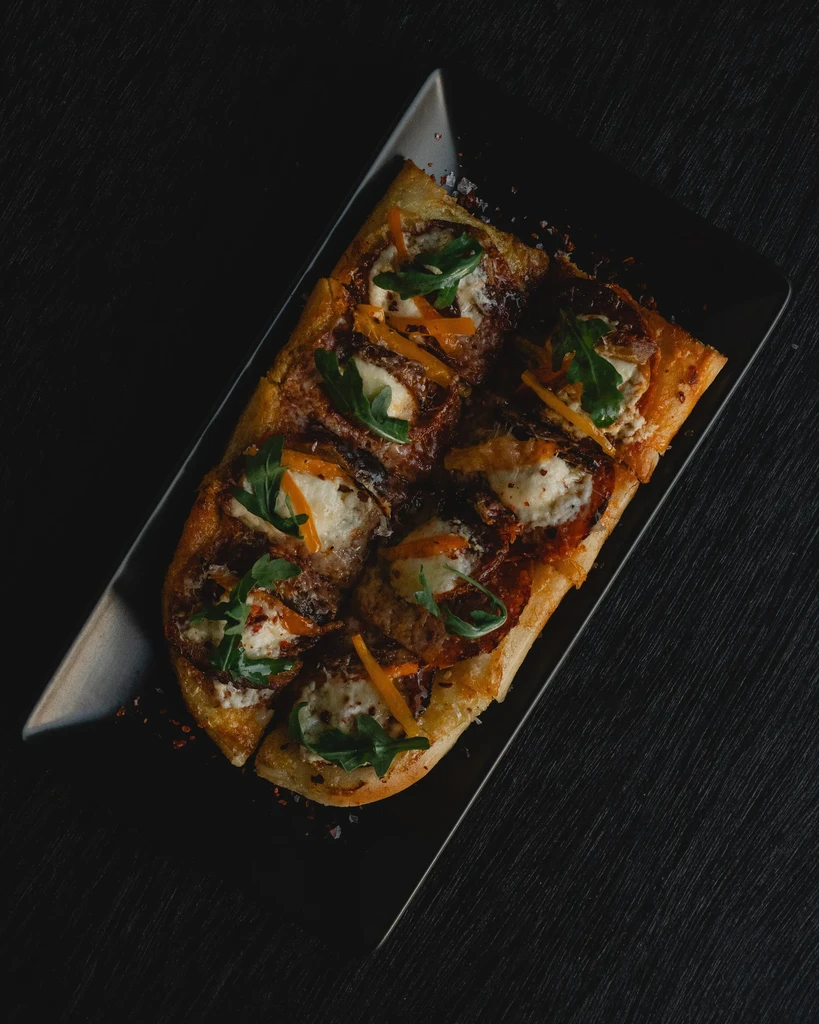 Sliced rectangular pizza with white cheese, green leaves, orange strips.