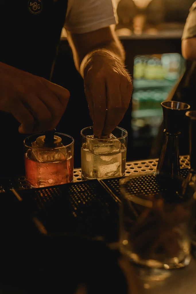 Bartender's hands preparing two drinks with large square ice.
