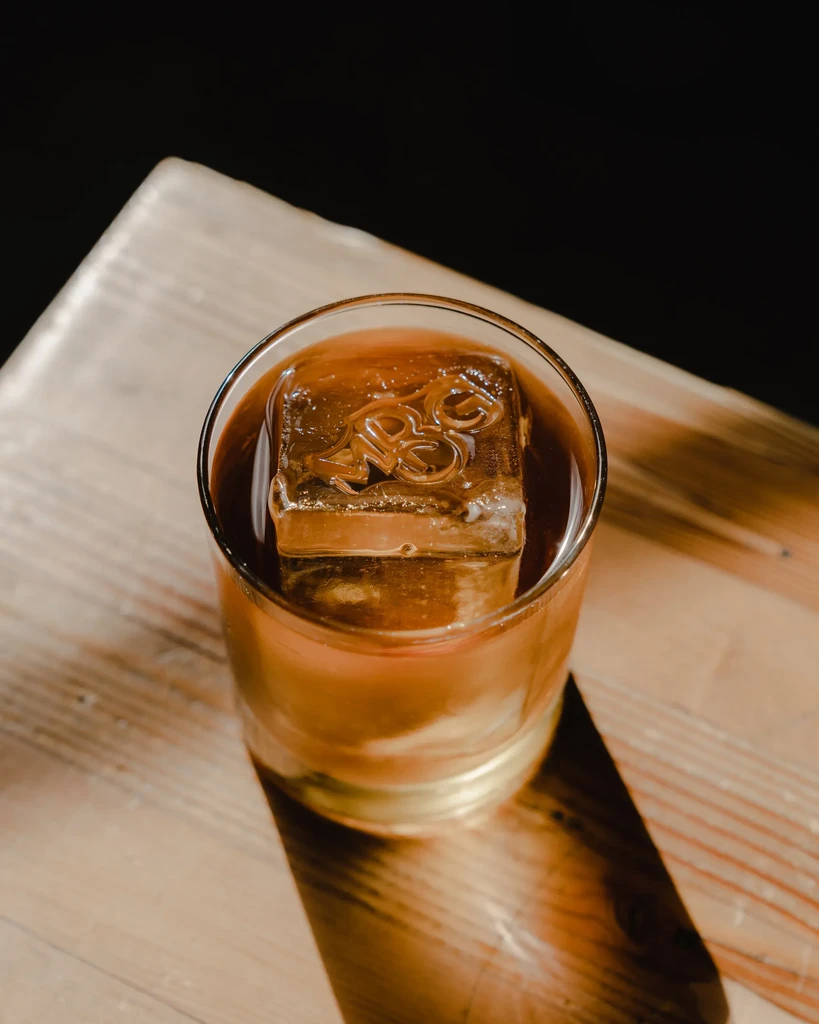 Close-up of amber cocktail with a square, logo-embossed ice cube.