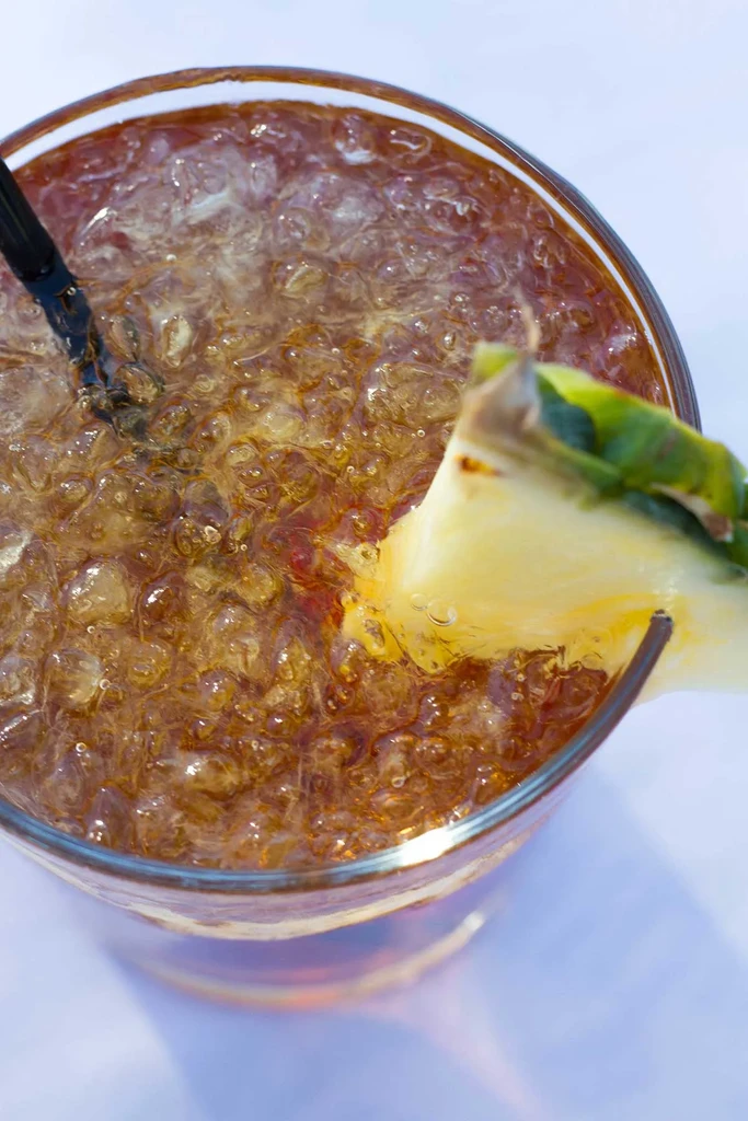 Close-up of amber iced drink with crushed ice, pineapple, and straw.
