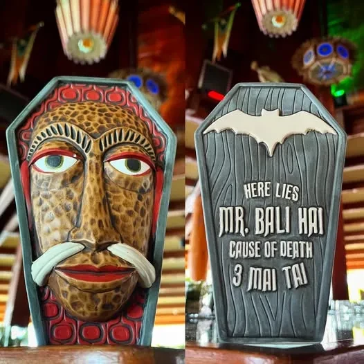 Tiki mask and a tombstone reading "Cause of Death 3 Mai Tai".
