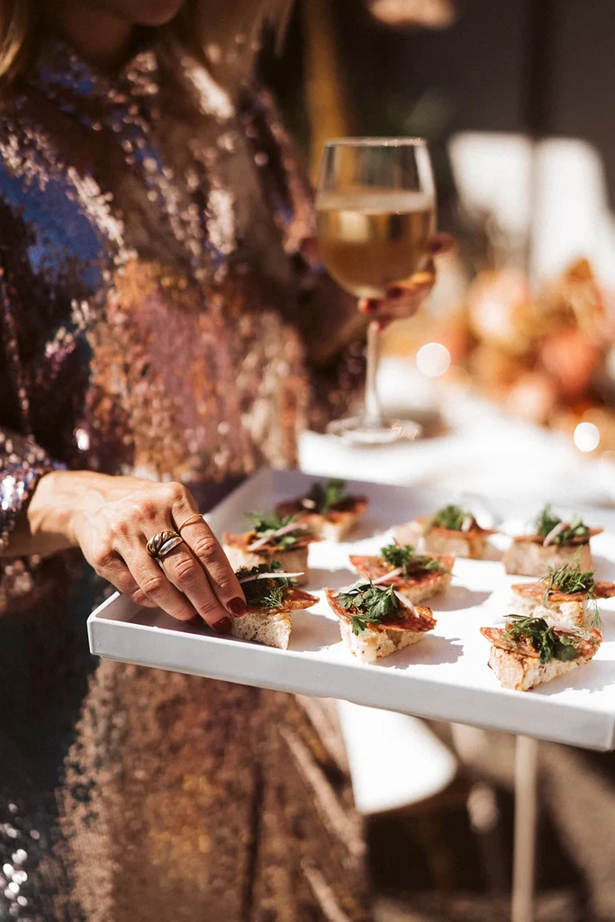 Hand reaching for a cured meat crostini from an appetizer tray.