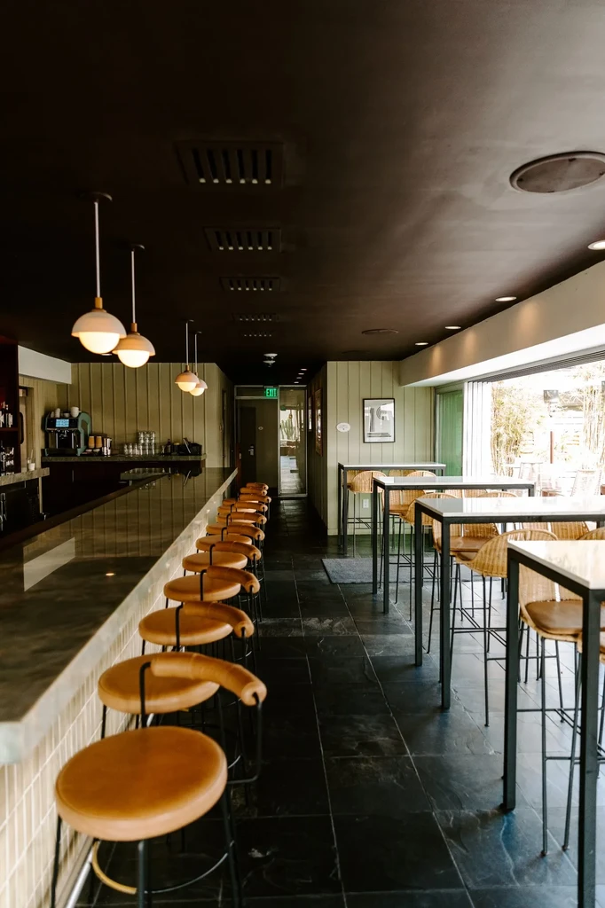 Modern bar with a long counter, high-top tables, and pendant lights.