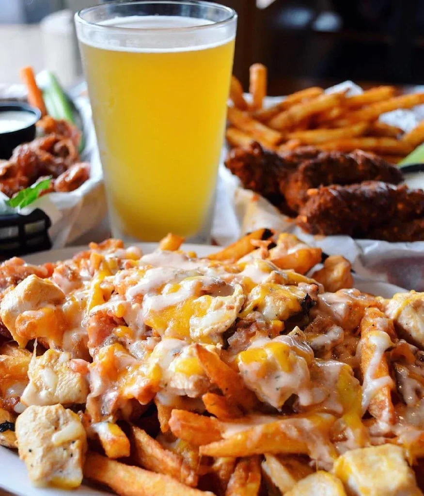 Close-up of loaded fries, beer, and chicken wings on a table.