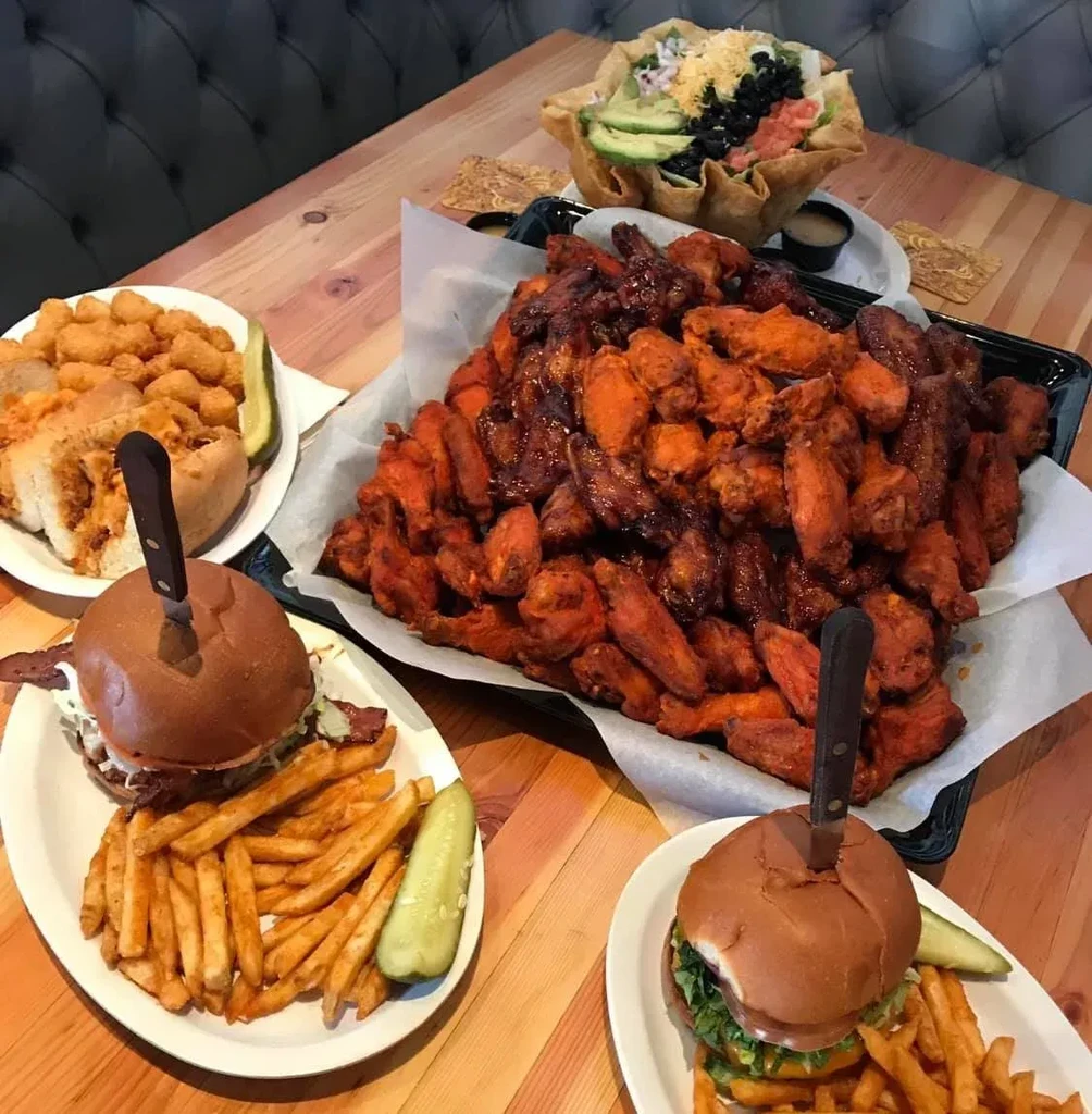 Restaurant table laden with burgers, fries, wings, sandwich, and taco salad.