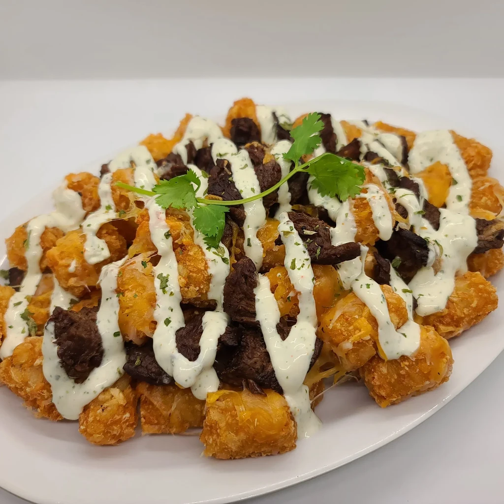 Tater tots with steak, herbed sauce, and cilantro.