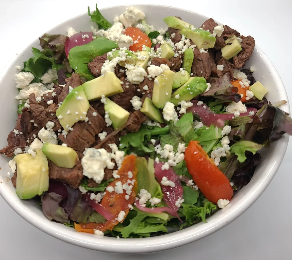 Steak salad with lettuce, avocado, cheese, and red onions.