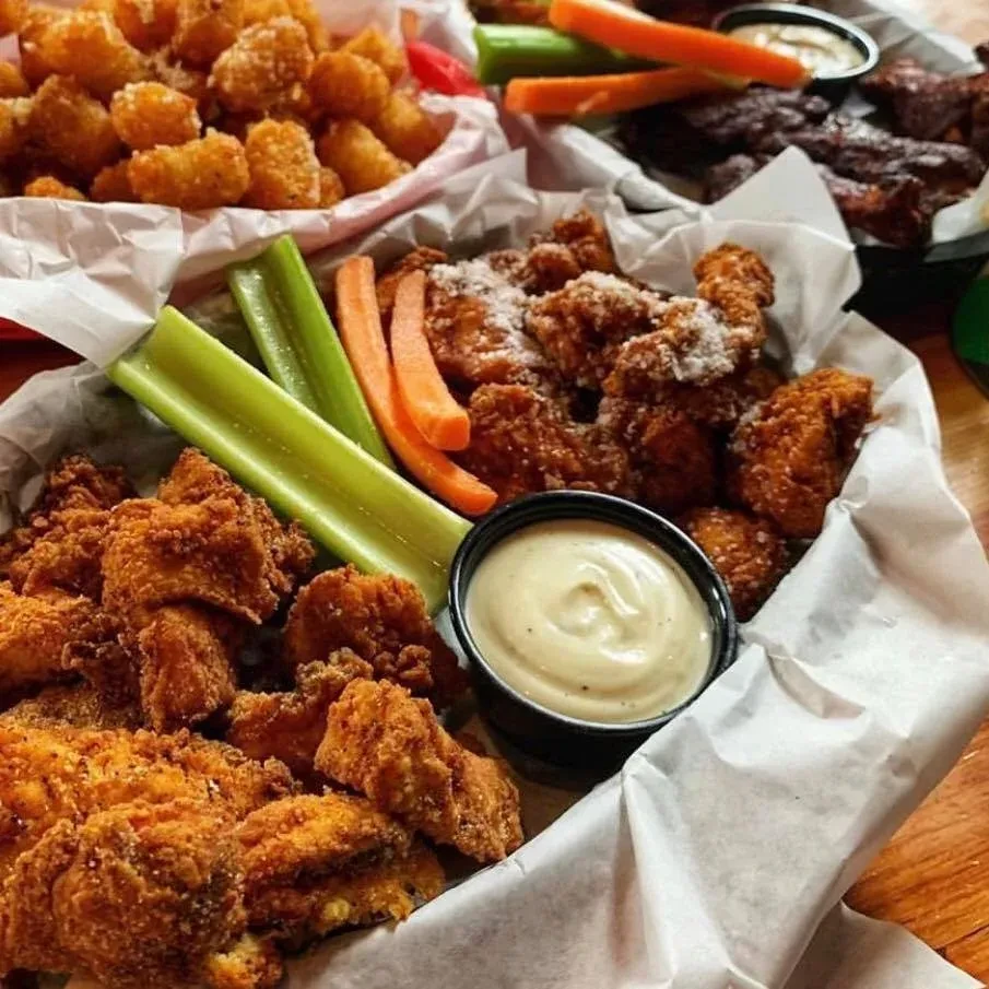 Close-up of fried chicken, vegetables, and dipping sauce in restaurant baskets.