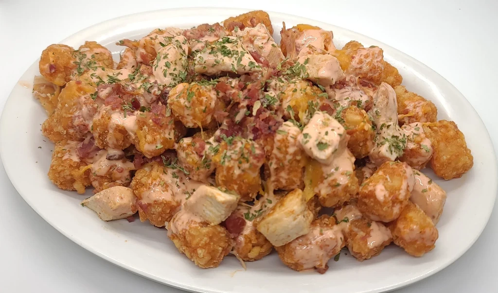 Loaded tater tots with chicken, bacon, creamy sauce, and green herbs.