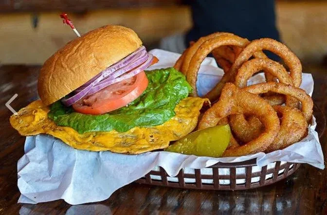 Gourmet burger, crispy onion rings, and pickle spear in a rustic basket.
