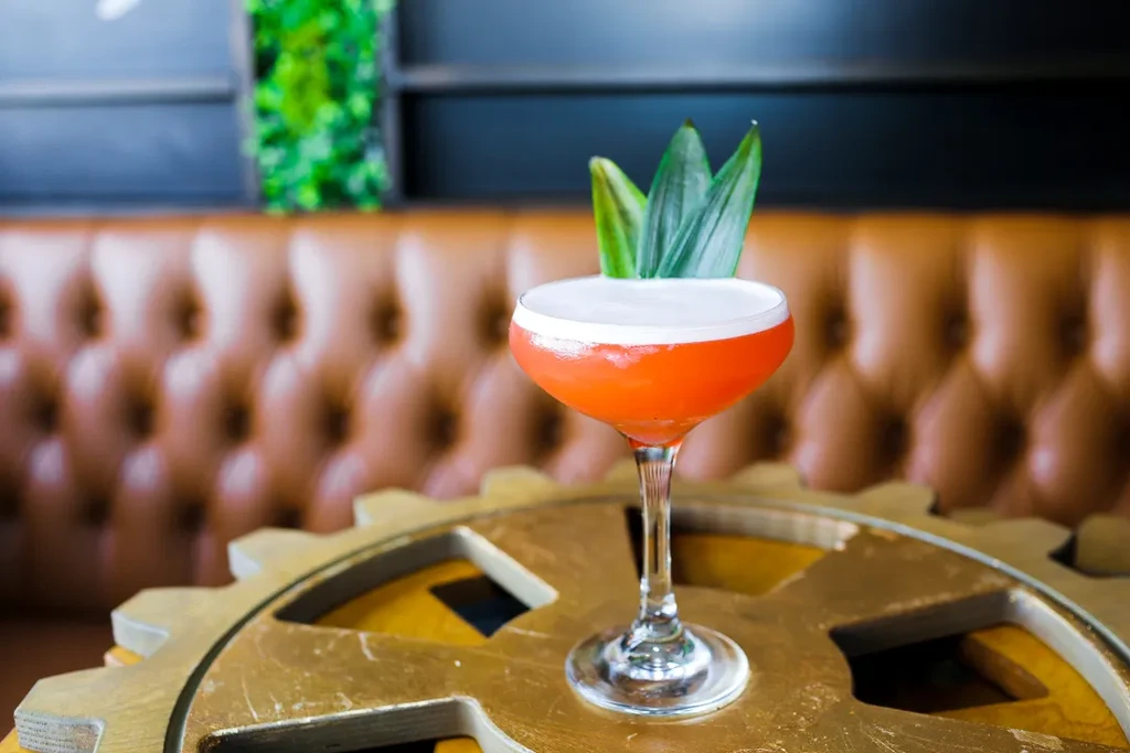 Orange cocktail with foam, green leaves, on golden gear table.