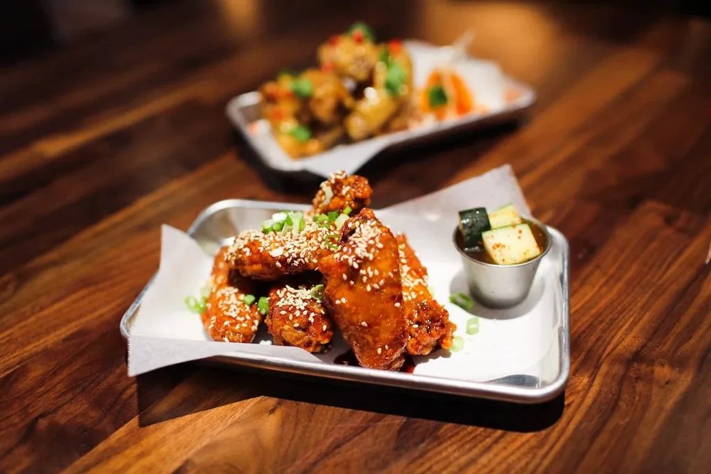 Sauced chicken wings with sesame, scallions, and cucumber on a metal tray.