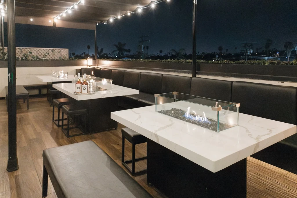 Nighttime outdoor dining with blue flame fire pits and city skyline.