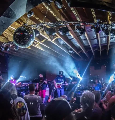 Audience view of a live band under blue lights with disco ball.
