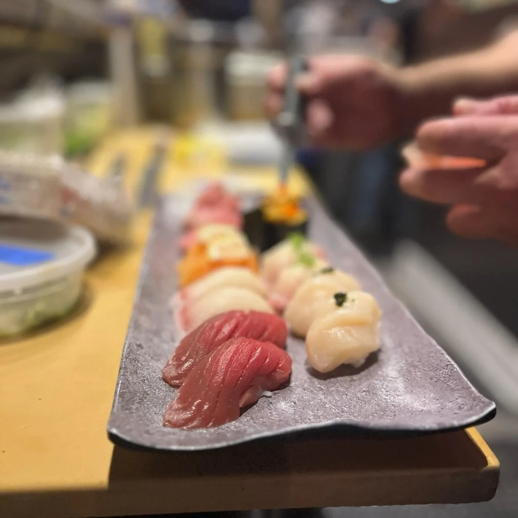 Nigiri sushi platter with prominent tuna; a chef's hands work in background.