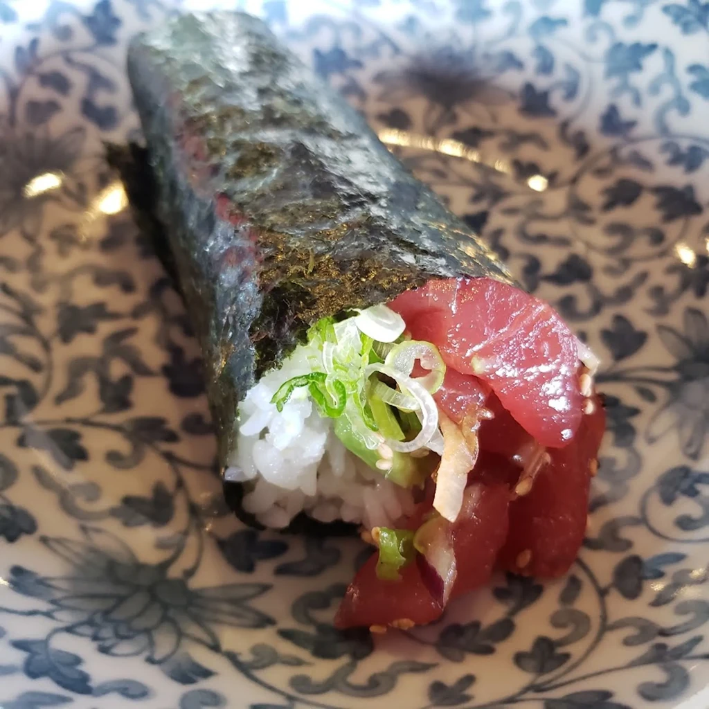 Close-up of a tuna hand roll with rice, nori, and green onions.