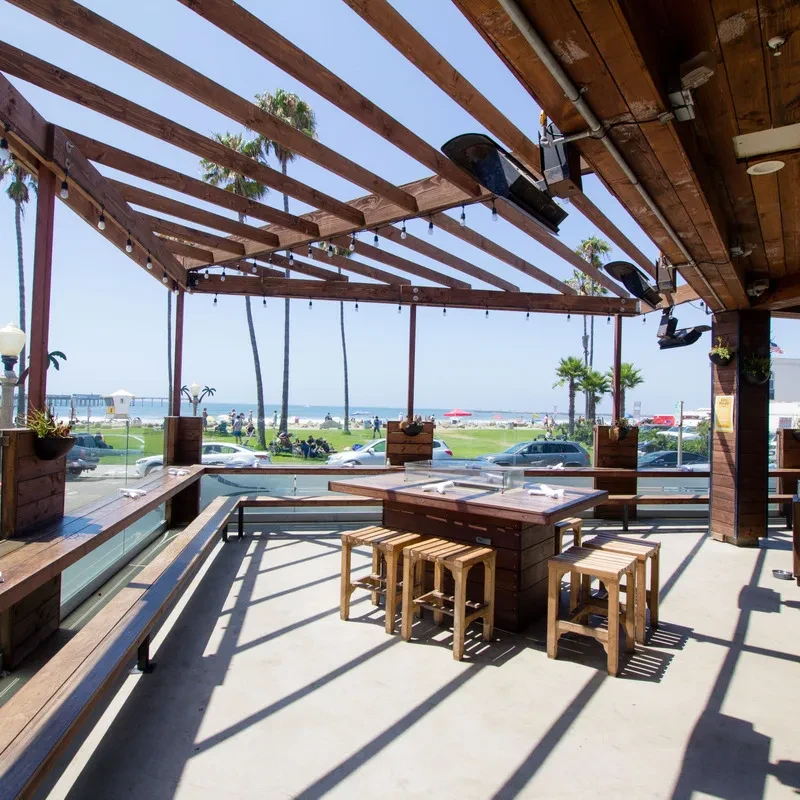 Restaurant patio with wooden pergola, communal table, and pier view.