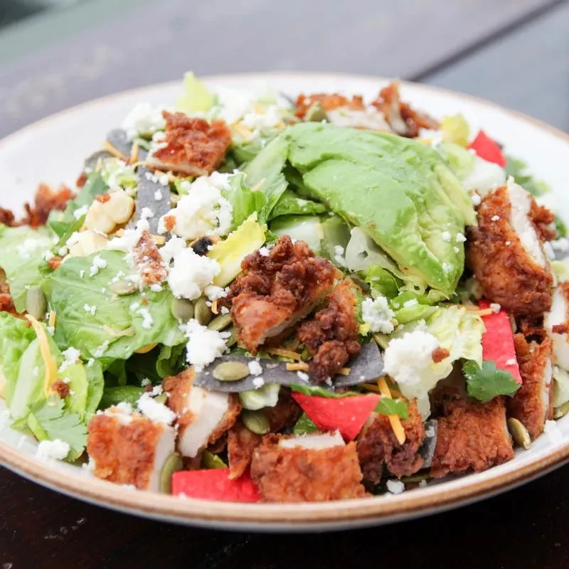Vibrant salad with crispy chicken, avocado, cheeses, pepitas, and tortilla strips.