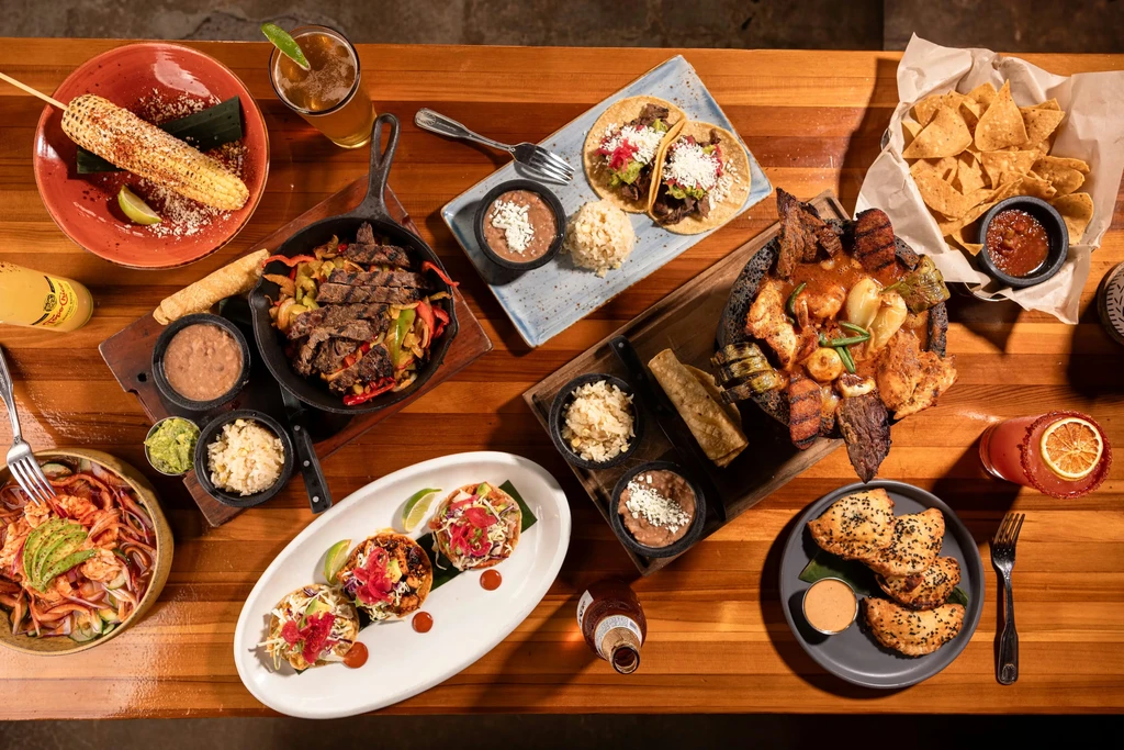 Overhead view of a wooden table laden with vibrant Mexican food and drinks.