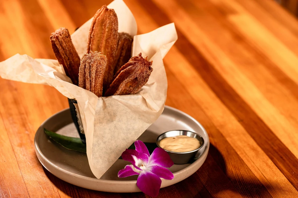 A basket of churros, dipping sauce, and a purple orchid.