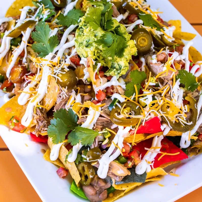 Plate of fully loaded nachos with meat, cheese, and guacamole.
