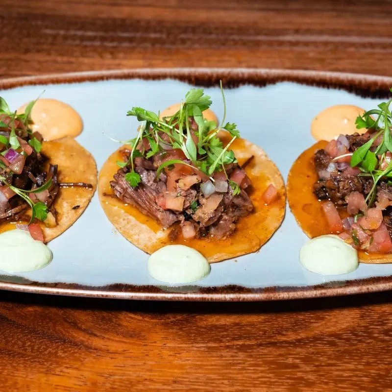 Three beef tacos with pico, microgreens, and green and orange sauces.