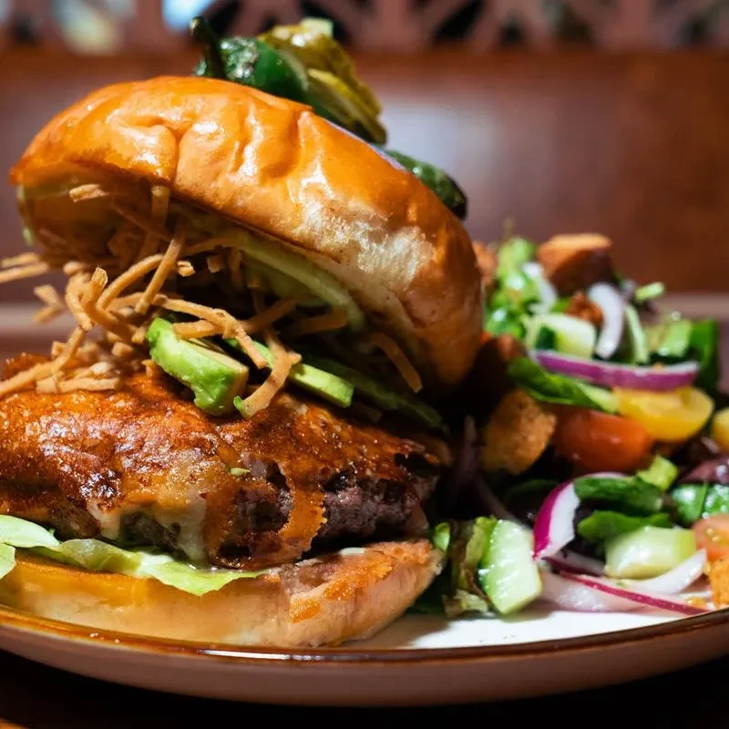 Gourmet burger with avocado, melted cheese, fries, and a side salad.