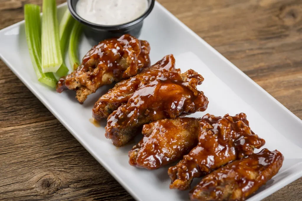 Chicken wings with dark sauce, celery, and white dip on rustic wood.