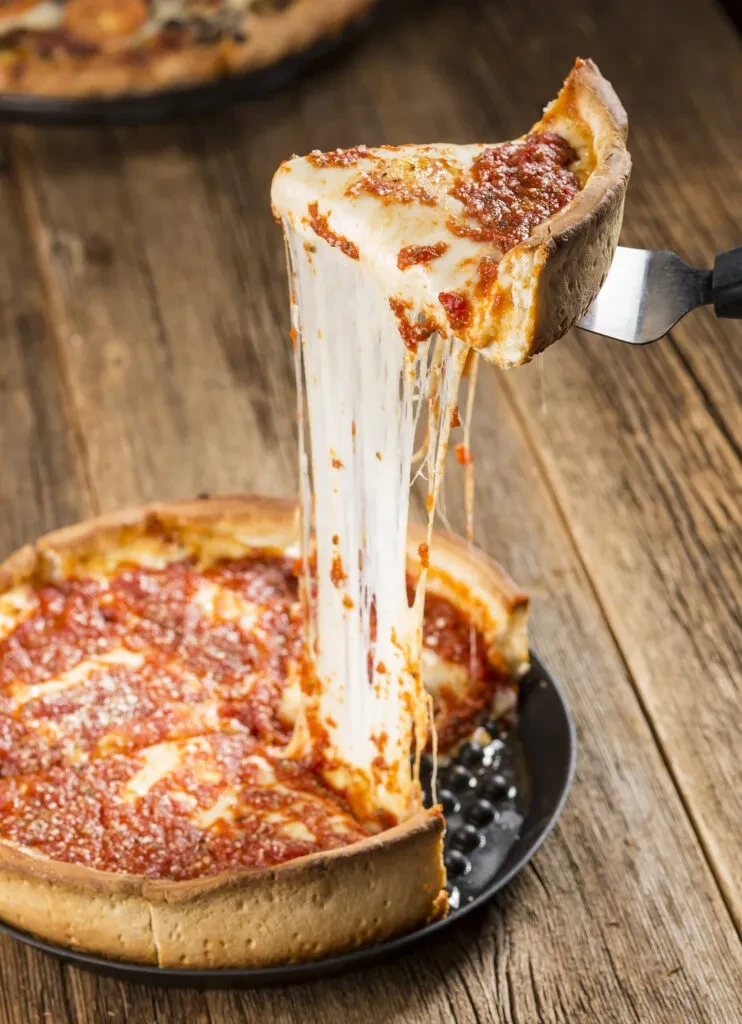 Deep-dish pizza on a wooden table with a long cheese pull.