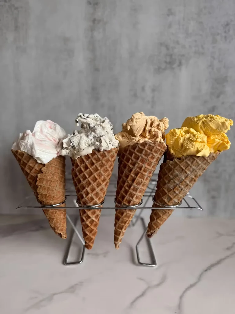 Four different-flavored ice cream cones in a silver stand on marble.