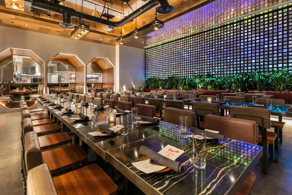Modern restaurant interior with communal table, booths, and colorful grid wall.