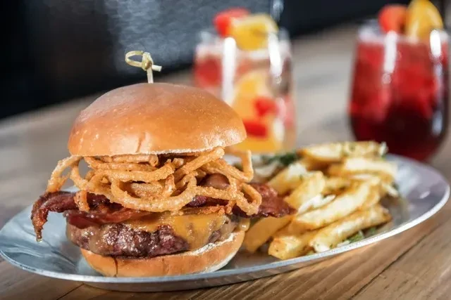 Gourmet burger with cheese, bacon, onion rings, and french fries.