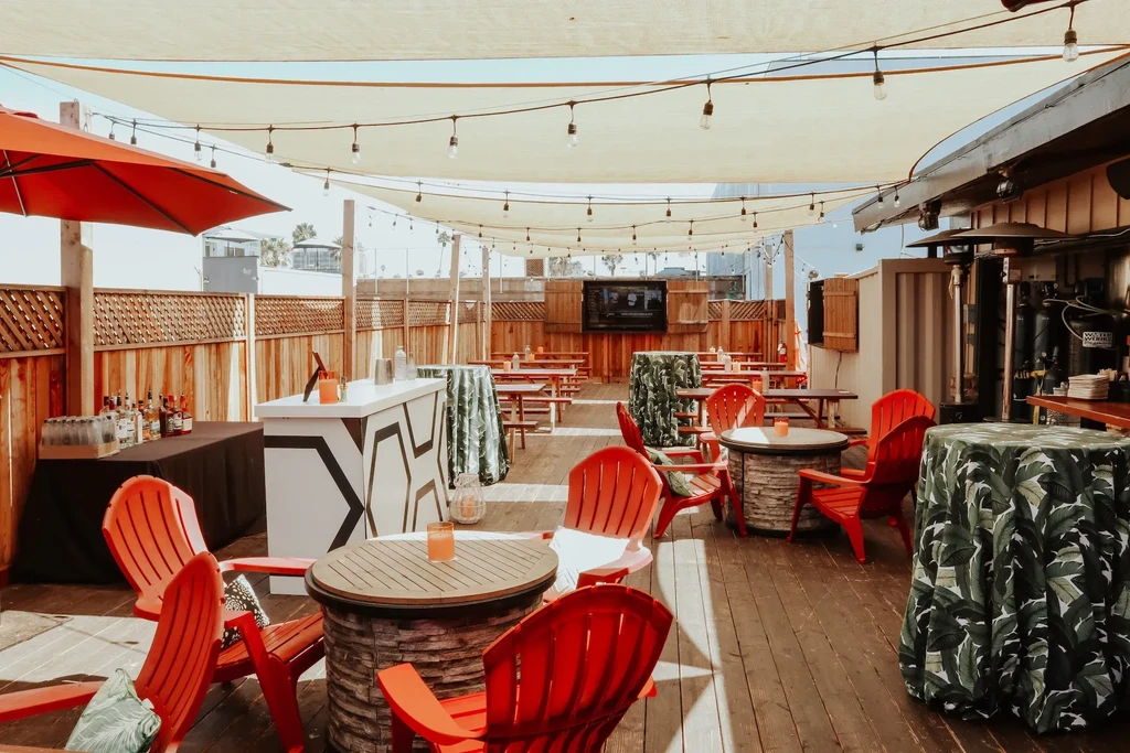 Daylit outdoor bar patio with red Adirondack chairs and tropical tablecloths.