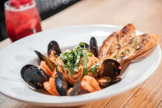 Seafood pasta with mussels, shrimp, and grilled bread in a white bowl.