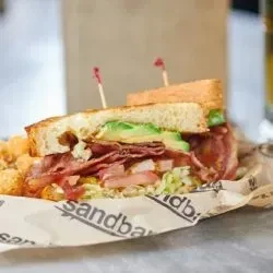 Club sandwich with bacon, avocado, lettuce, tomato, tater tots, cut diagonally.