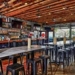 Empty modern rustic bar interior with communal tables and wood beams.