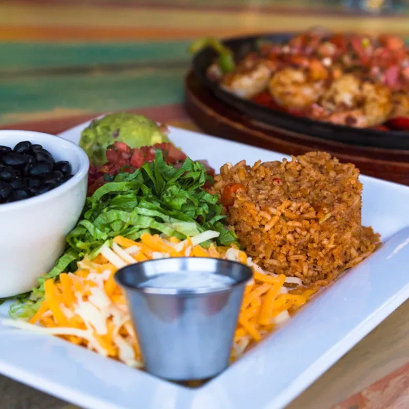 Tex-Mex plate with rice, beans, cheese, guacamole, and sizzling fajitas behind.