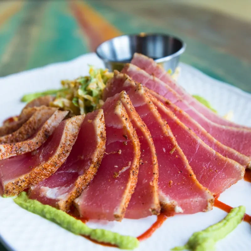 Close-up of fanned seared tuna with shredded greens and two sauces.