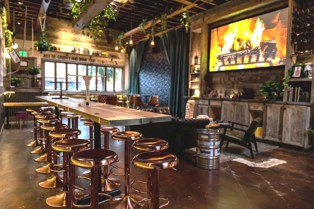 Rustic bar interior with long communal table and large fireplace screen.