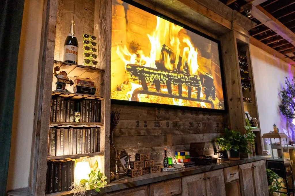 Rustic interior with a digital fireplace screen, bookshelf, and wine bottles.
