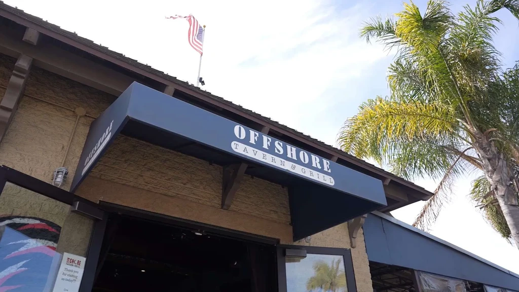 Offshore Tavern & Grill exterior, blue awning, American flag, palm tree.