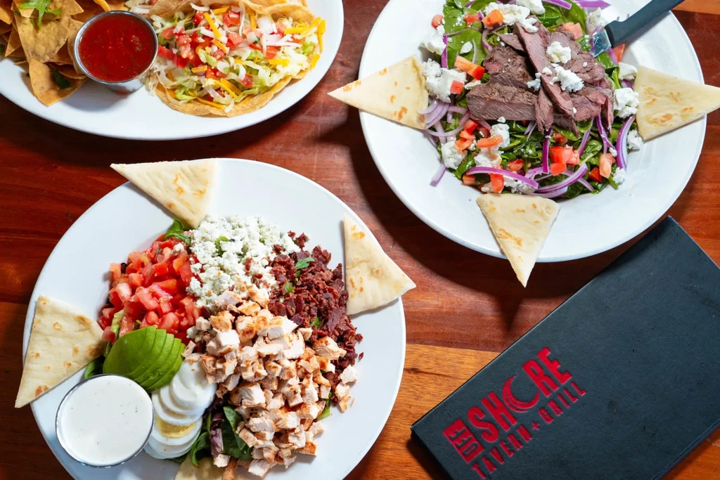 Three plates of Mexican and American food on a wooden restaurant table.
