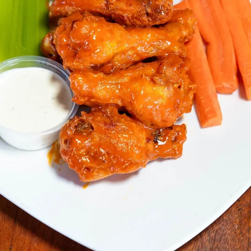 Glistening buffalo chicken wings, dipping sauce, and carrots on a plate.