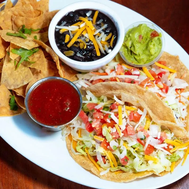 Plate of two crispy tacos, tortilla chips, black beans, guacamole, salsa.