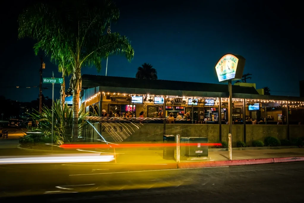 Bustling 'Old Shore' restaurant at night with car light trails.