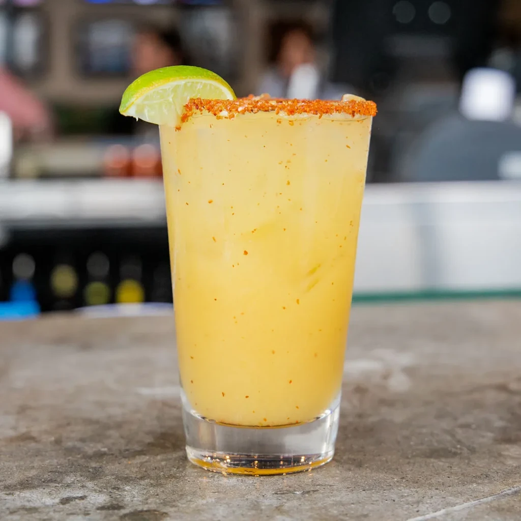 Frothy yellow-orange drink with chili-salt rim and lime wedge.