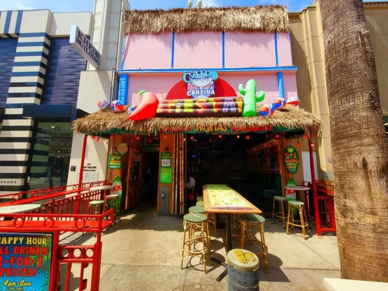 Pink Cabo Cantina restaurant with thatched roof, inflatables, and Happy Hour sign.