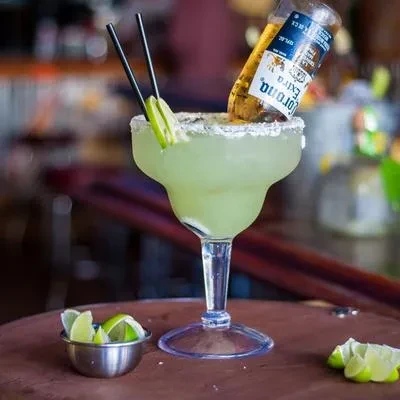 Salt-rimmed green margarita with an inverted Corona bottle and lime.