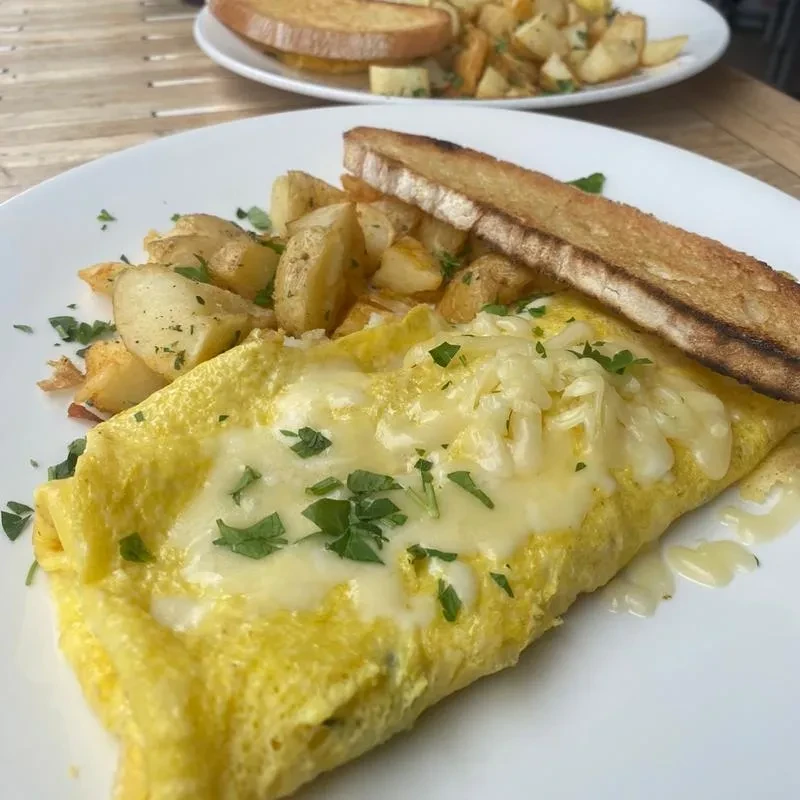 Golden omelet with cheese and parsley, roasted potatoes, and toast.